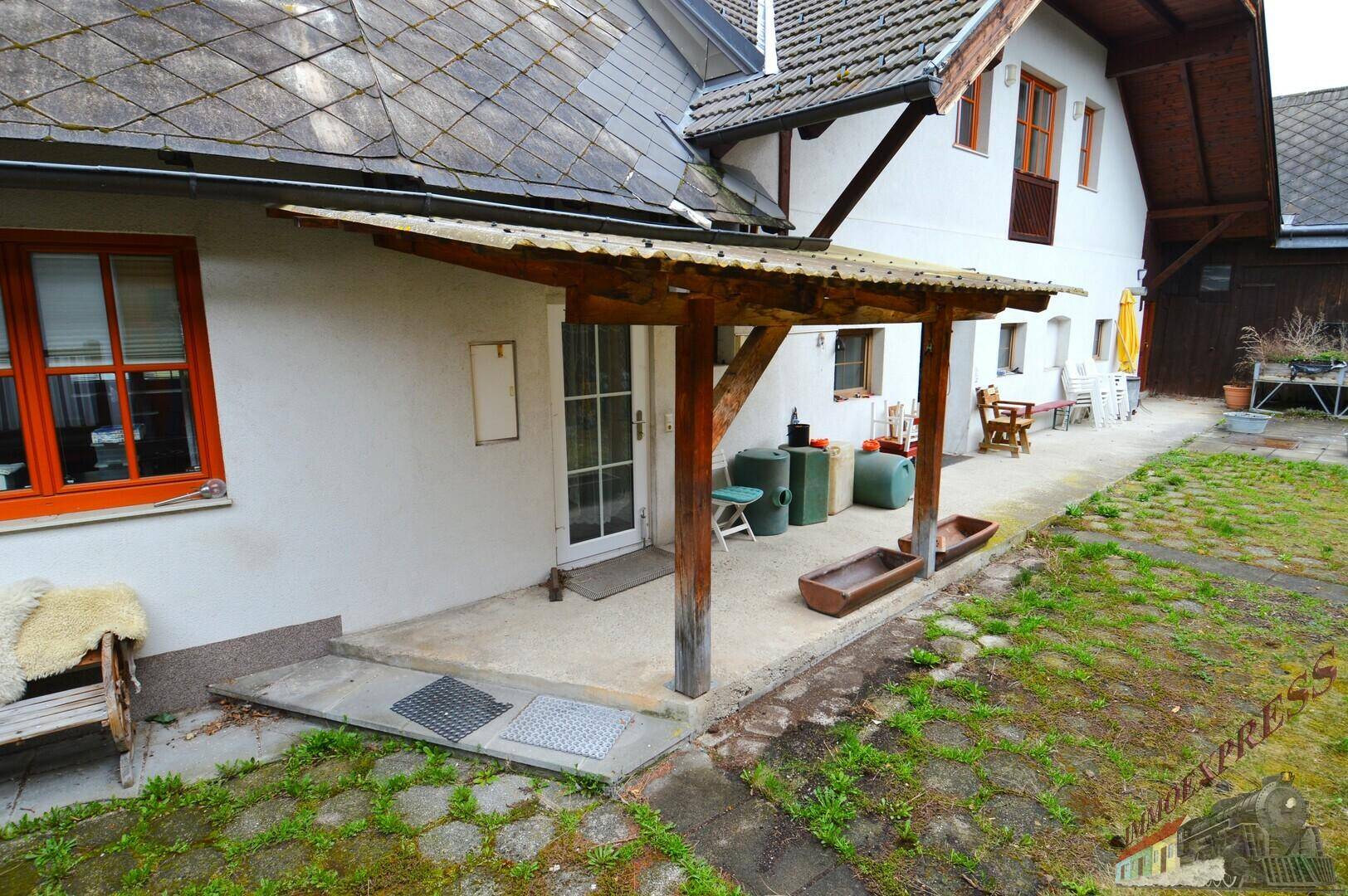 Überdachter Eingangsbereich mit Sitzbank und Zugang zum Garten, umgeben von ländlicher Architektur.