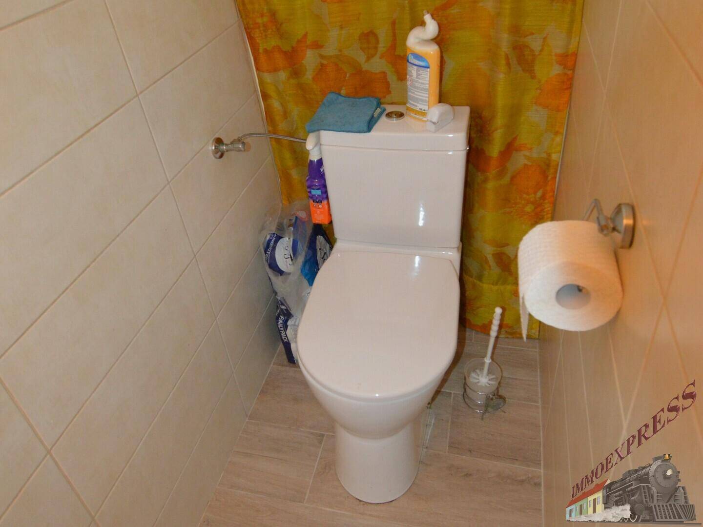 Einfaches WC mit Steh-WC, Fliesenboden und einer gelb-orangen Duschvorhang.