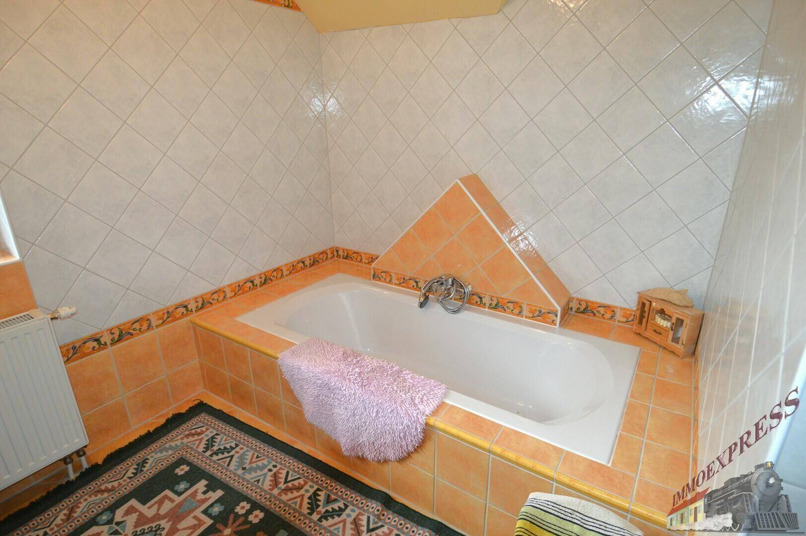 Badewanne in einem Badezimmer mit orange-weißen Fliesen und einem traditionellen Teppich auf dem Boden.