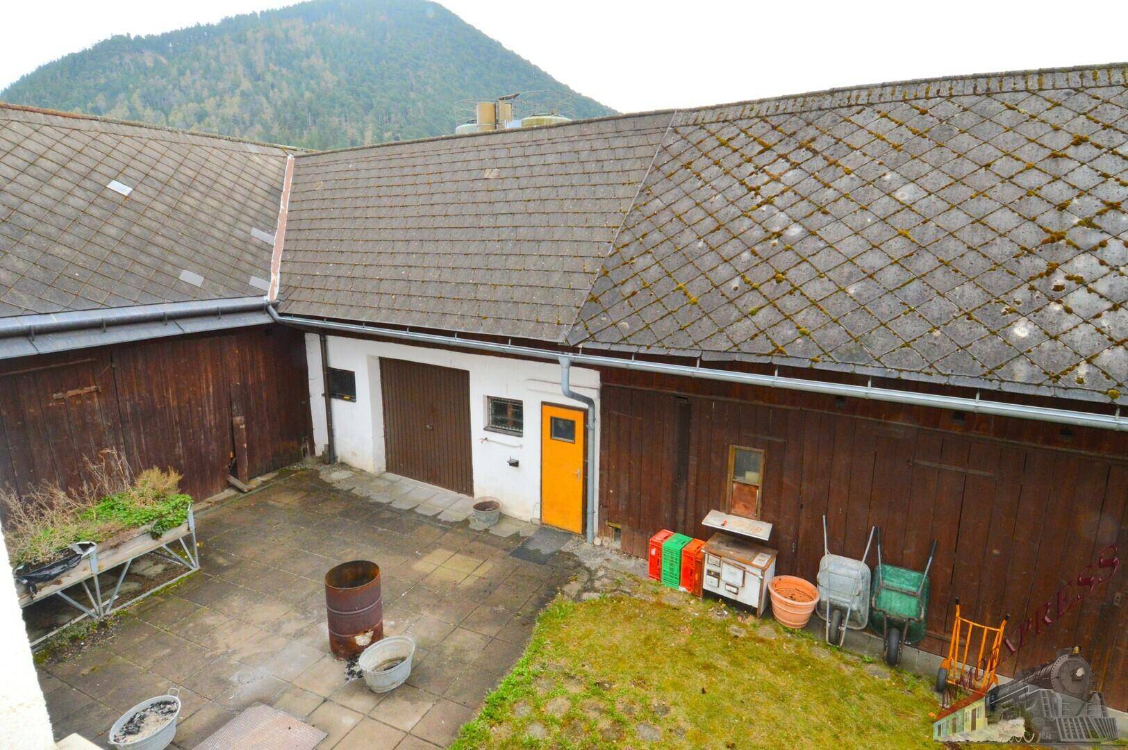 Blick von oben auf den Innenhof mit gepflasterter Fläche, Nebengebäuden und umgebenden Dächern.