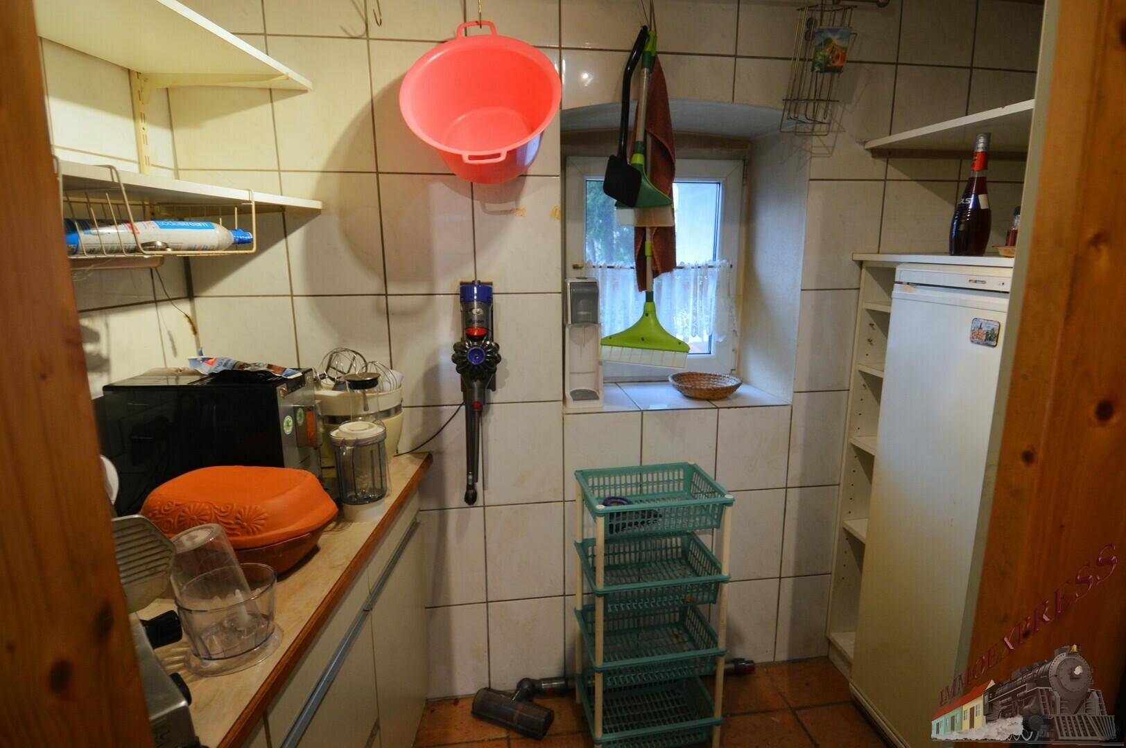Kleiner Abstellraum mit Fliesen, Regalen und einem Fenster, der als Waschküche genutzt werden könnte.