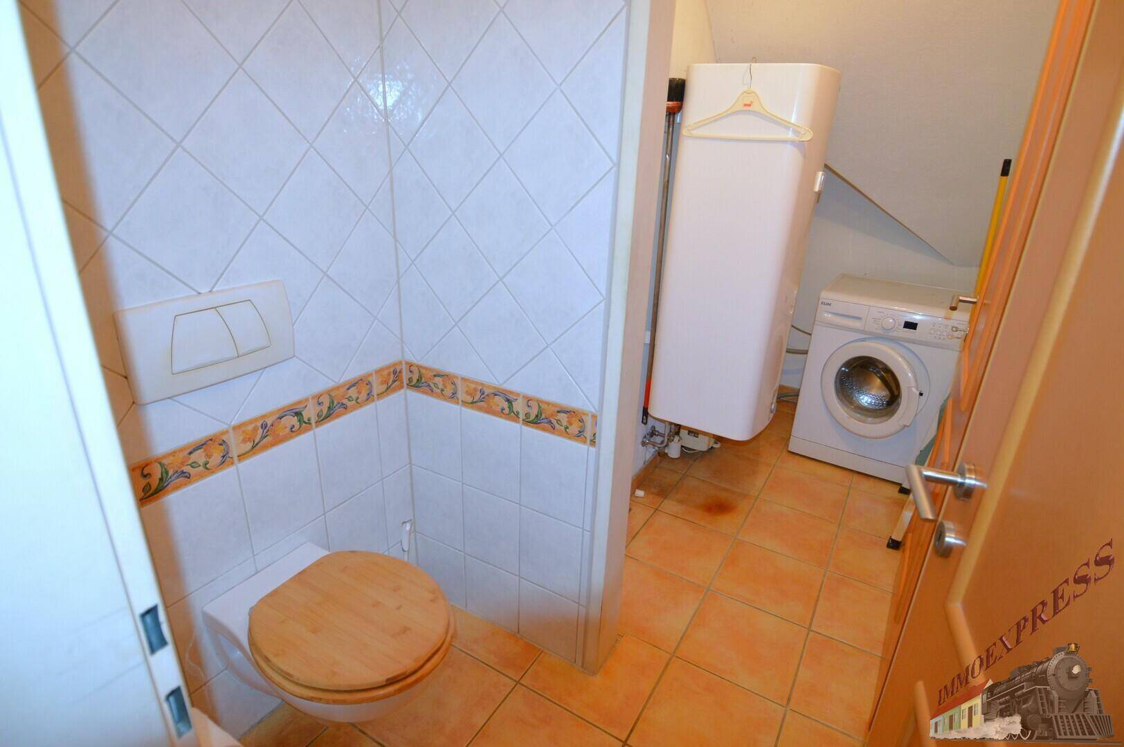 Separate Toilette mit Waschmaschine und Trockner, gefliest in orange-weißen Farbtönen.