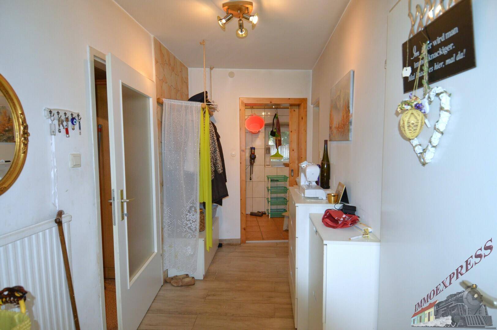 Heller Flur mit Holzfußboden, Garderobe und Spiegel, der zu weiteren Räumen führt.