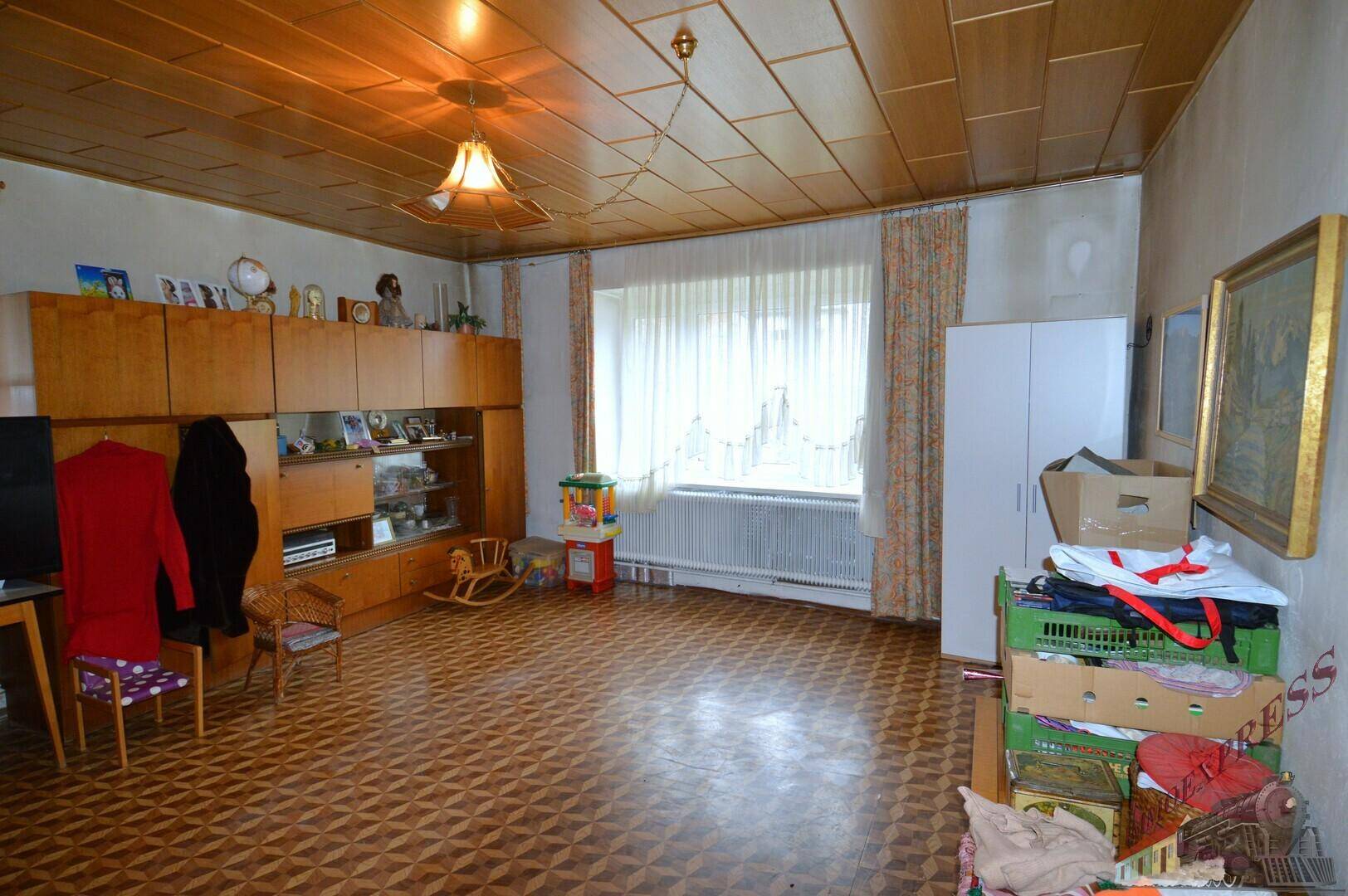 Geräumiges Wohnzimmer mit Holzdecke, gemustertem Boden und einem großen Fenster.