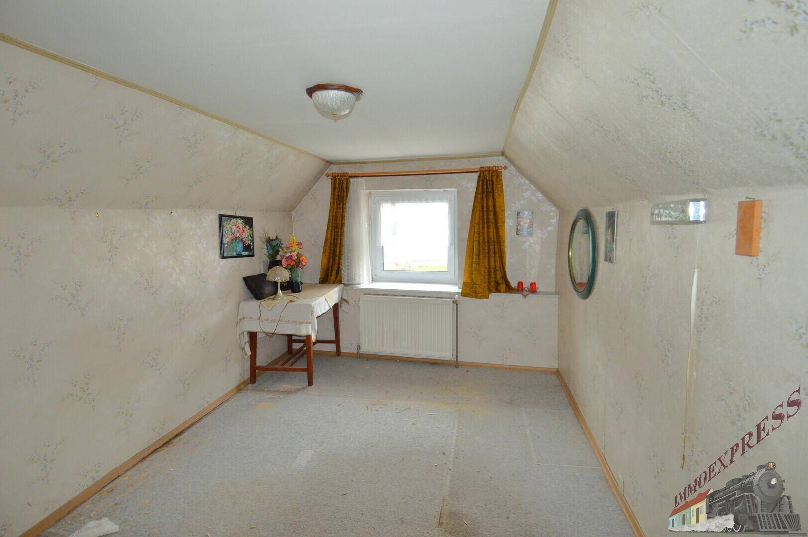 Dachzimmer mit schrägen Wänden, Tapete und einem Fenster, das viel Licht hereinlässt.