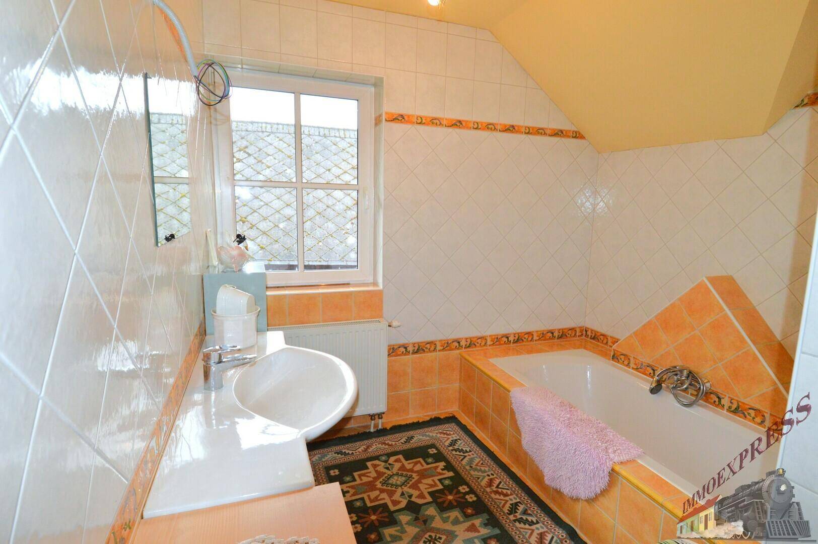Helles Badezimmer mit Fenster, Badewanne, Waschbecken und orange-weißen Fliesen im traditionellen Stil.
