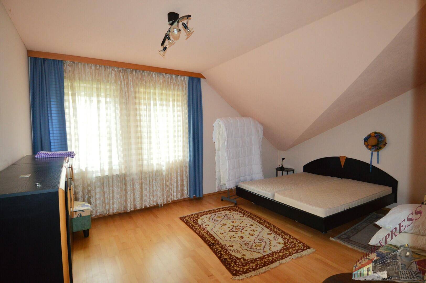 Schlafzimmer im Dachgeschoss mit Holzboden, Doppelbett und schräger Decke, hell durch große Fenster.