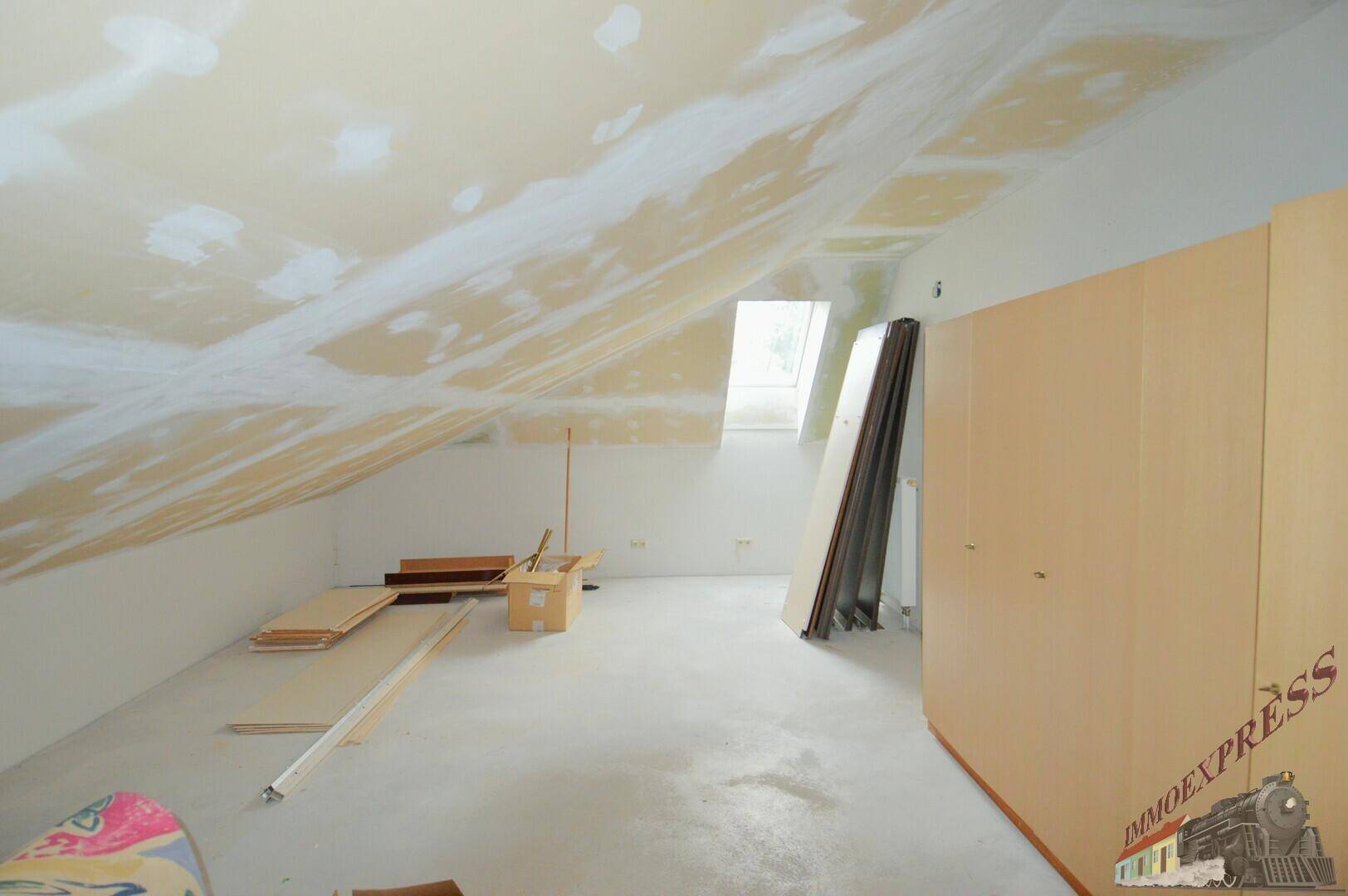 Unausgebauter Dachbodenraum mit schrägen Wänden und Dachfenster, bereit für den Ausbau.