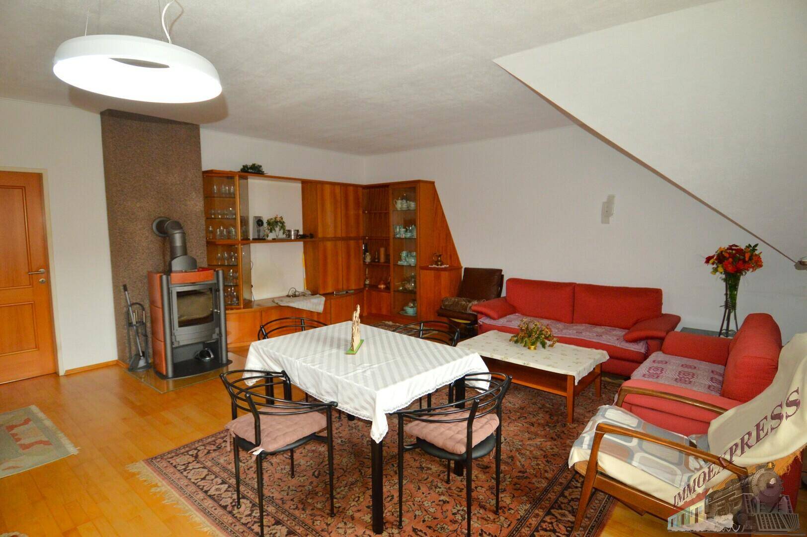 Gemütlicher Wohn-Essbereich mit Holzboden, Kaminofen und traditionellen Möbeln unter schräger Decke.
