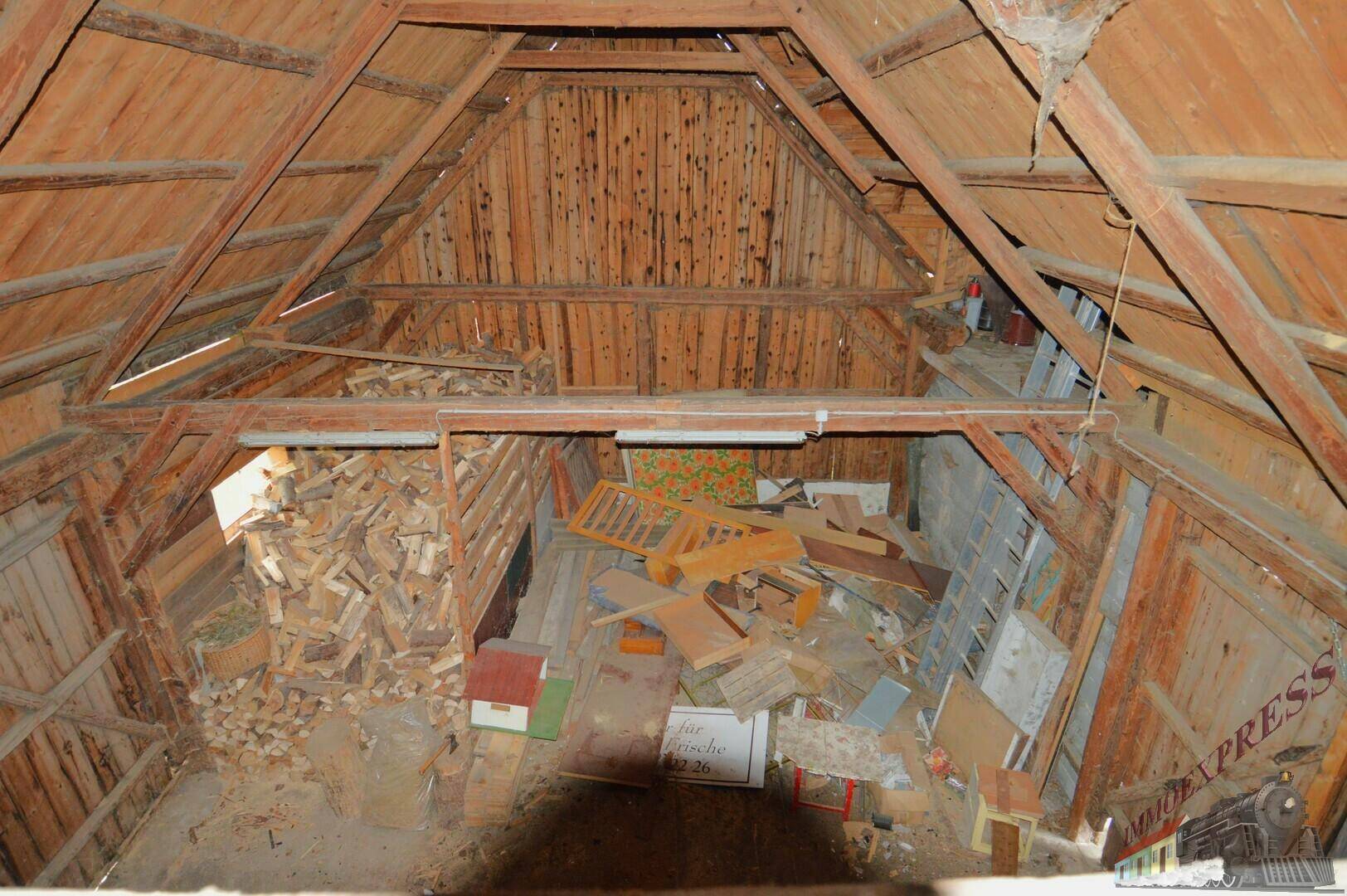 Dachboden oder Scheune mit sichtbaren Holzbalken und einem großen Stapel Brennholz.
