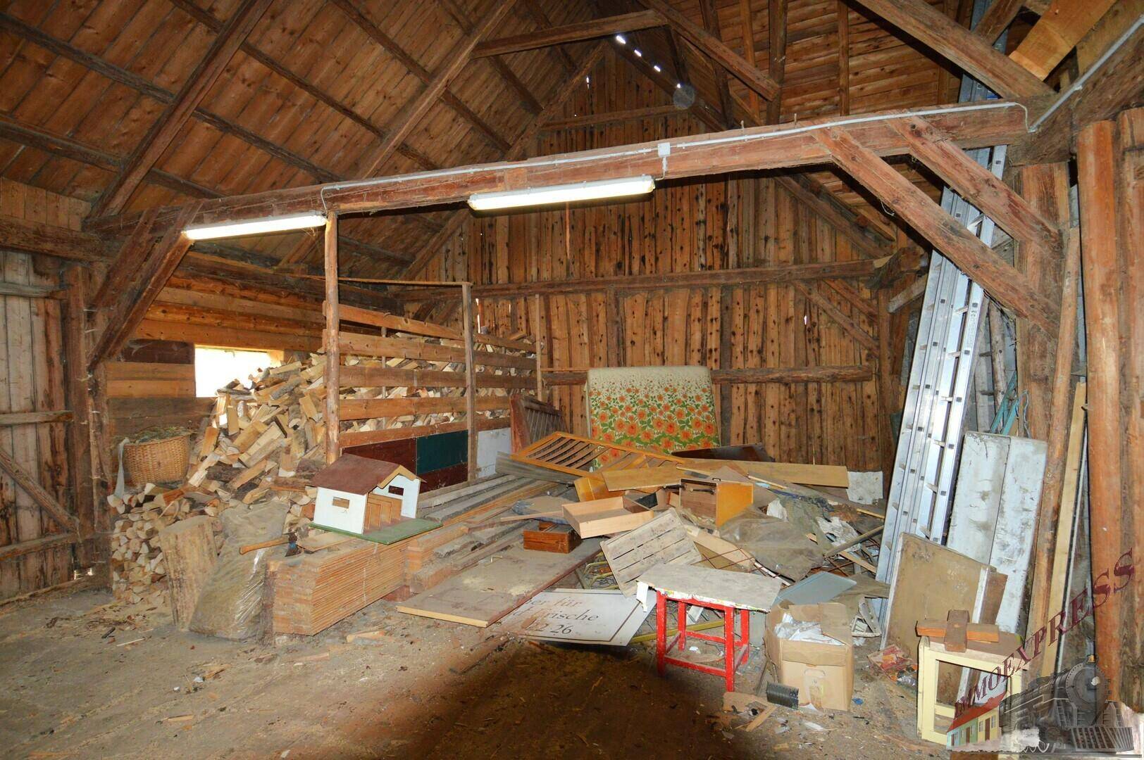 Große Scheune mit Holzbalken und gelagertem Brennholz, bietet viel Stauraum.