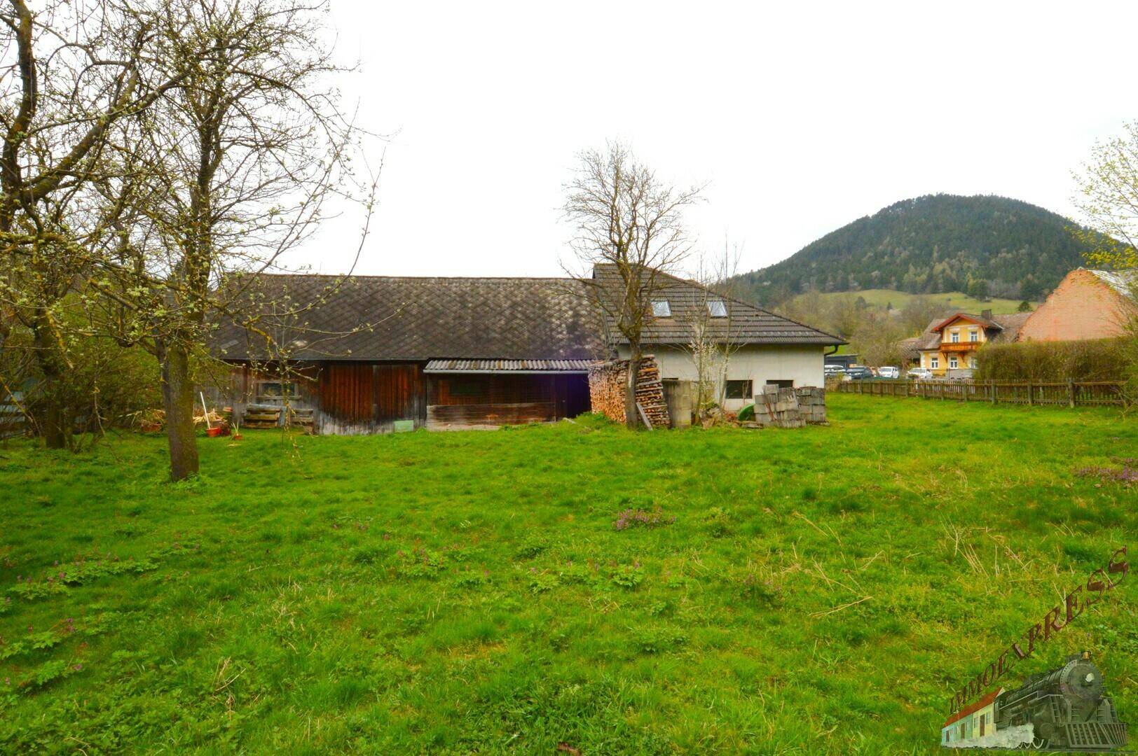 Panoramablick auf das Anwesen mit Haus, Scheune, weitläufigem Rasen und Bergblick im Hintergrund.