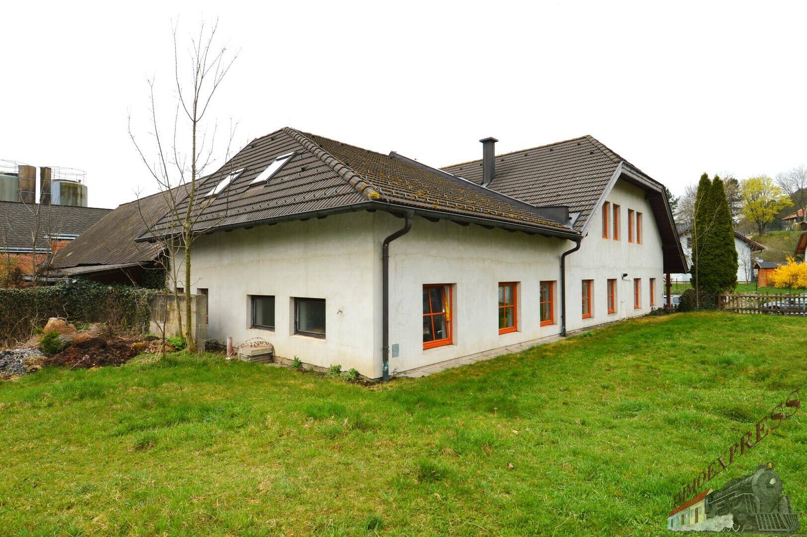 Seitenansicht des weißen Hauses mit orangefarbenen Fenstern, grünem Rasen und Dachfenstern.