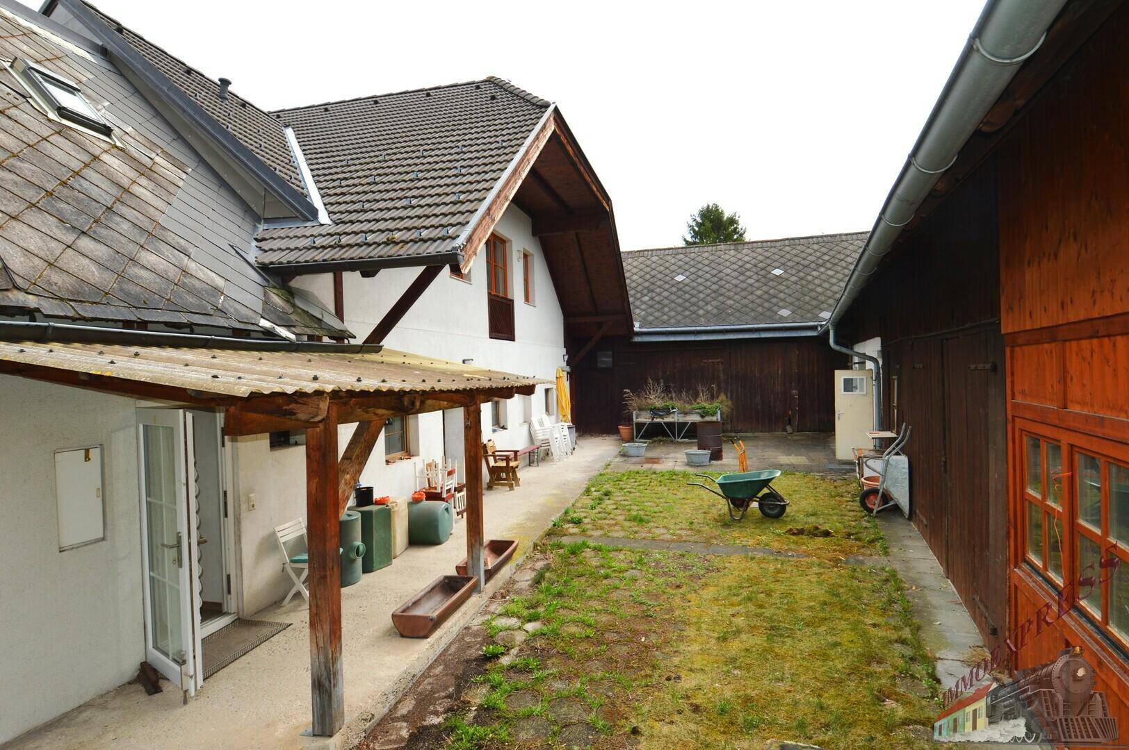 Ländlicher Innenhof mit Rasenfläche, Nebengebäuden und einem überdachten Eingangsbereich.