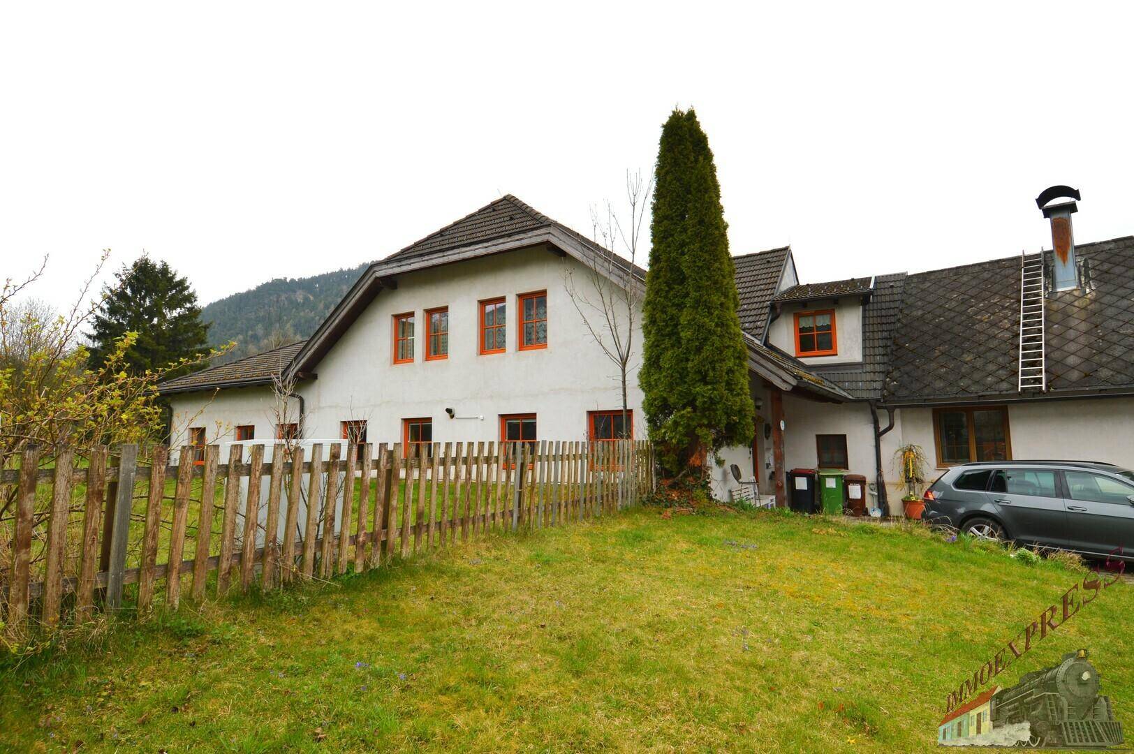 Ländliches Wohnhaus mit weißer Fassade, Holzzaun und großem Gartenbereich, umgeben von grüner Natur.