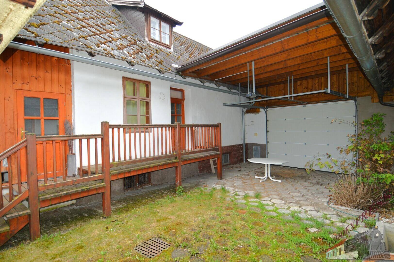 Hinterhofbereich mit Garage, Holzterrasse und einem kleinen gepflasterten Sitzbereich.