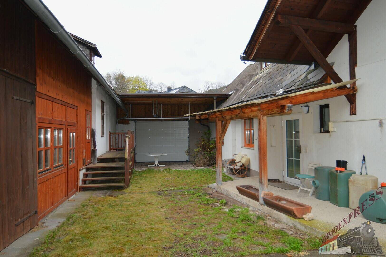 Ansicht eines ländlichen Anwesens mit mehreren Gebäuden, Garage und einem grünen Hofbereich.