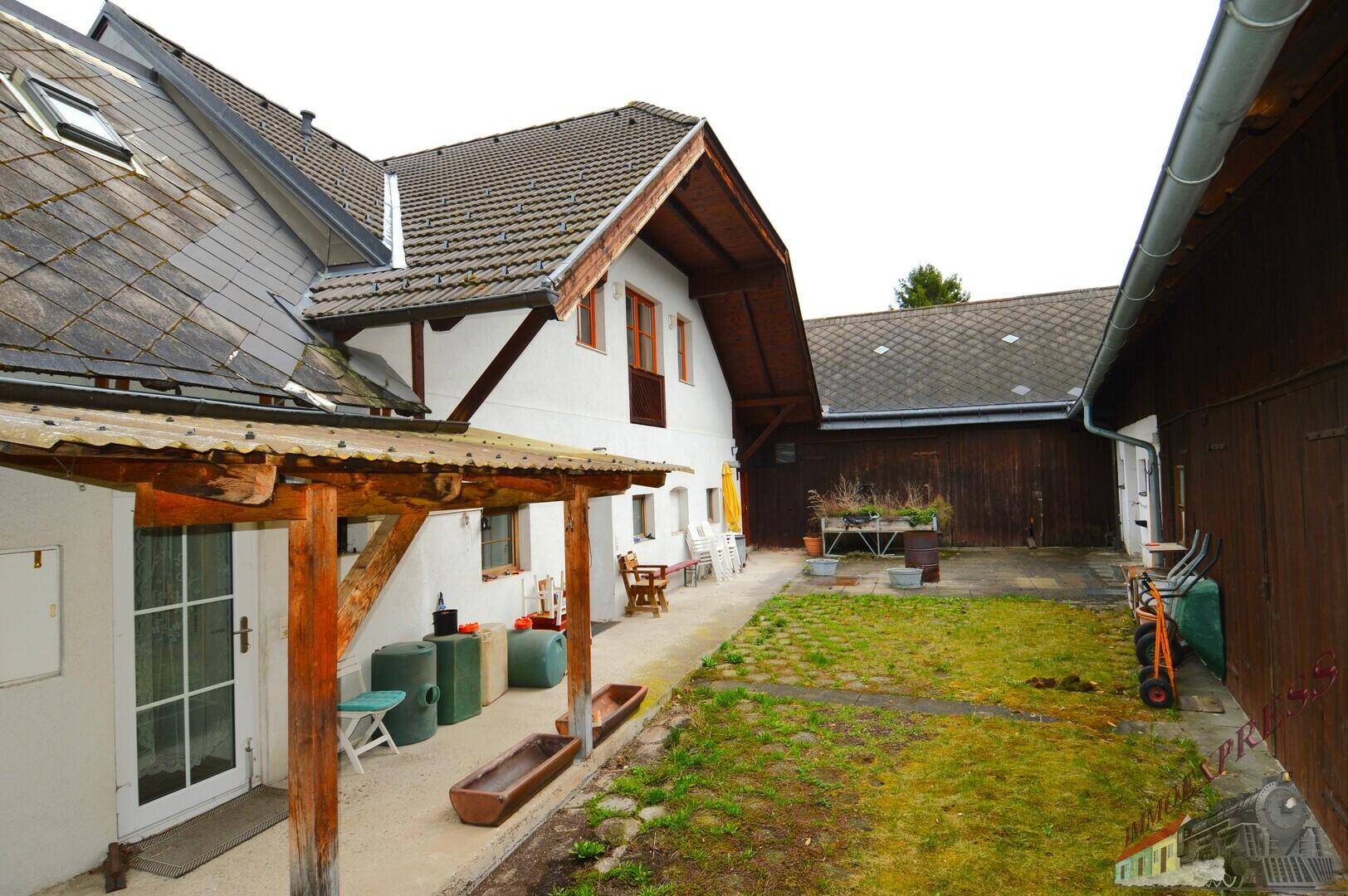 Innenhof mit Rasenfläche, überdachtem Eingangsbereich und Gartenmöbeln zwischen den Gebäuden.
