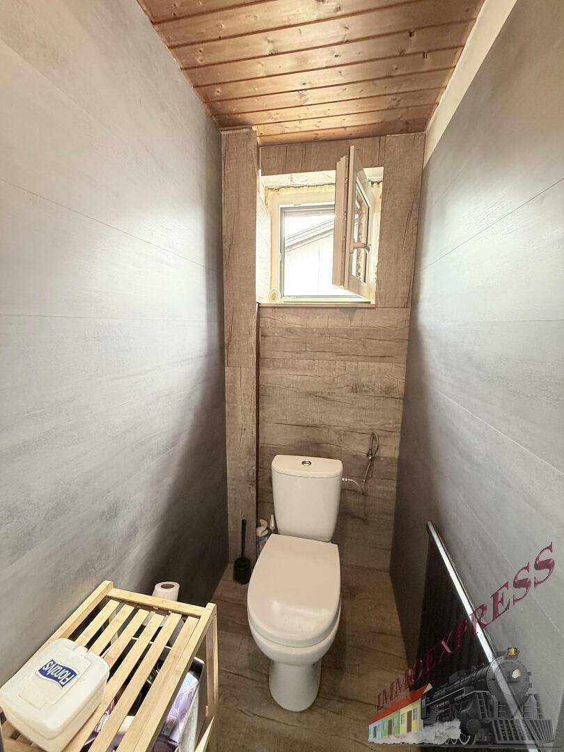 Kleines WC mit Toilette, kleinem Fenster und holzverkleideten Wänden und Decke.