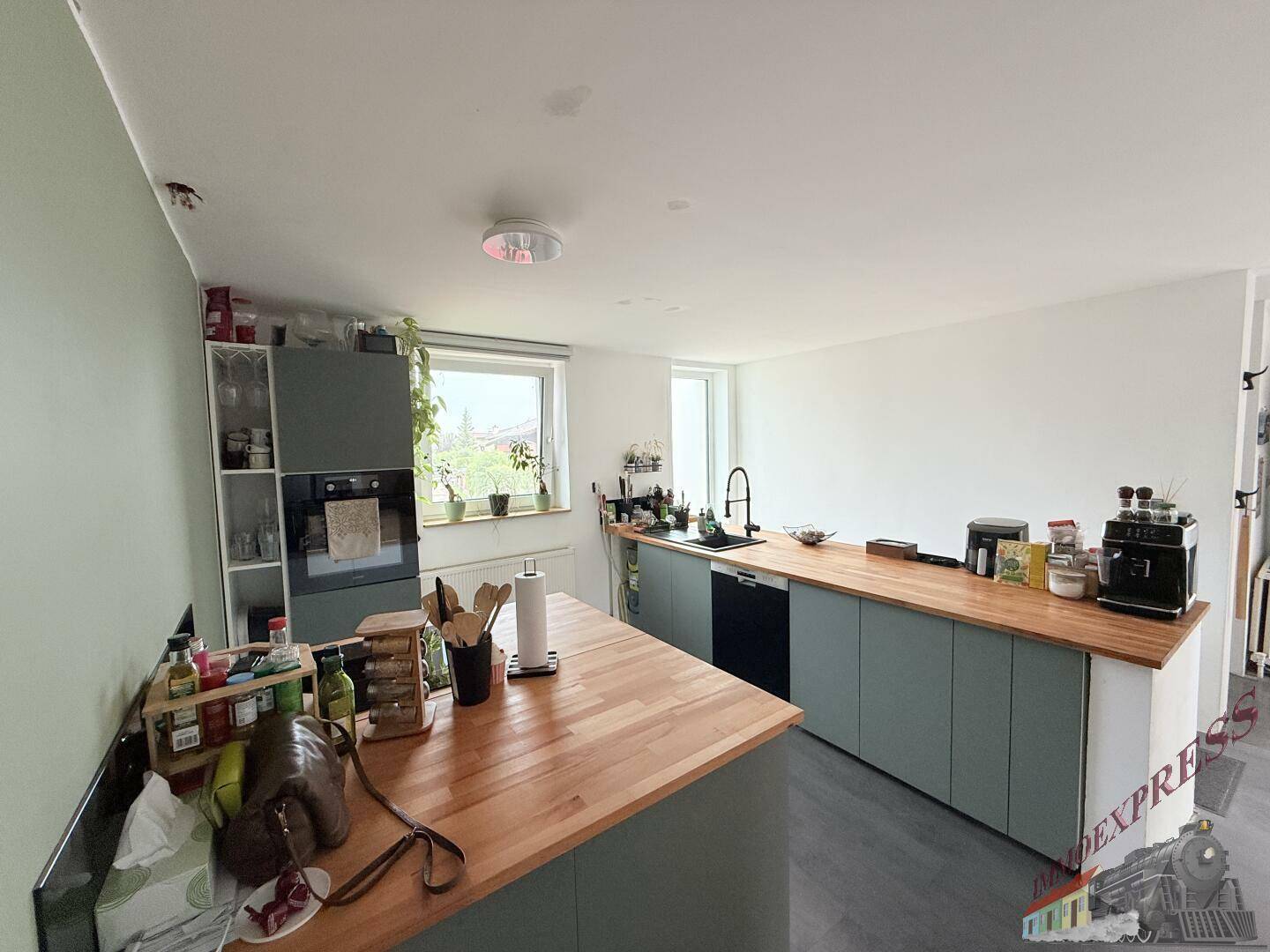 Moderne Küche mit hellgrünen Unterschränken, Holzarbeitsplatten und Fenster.