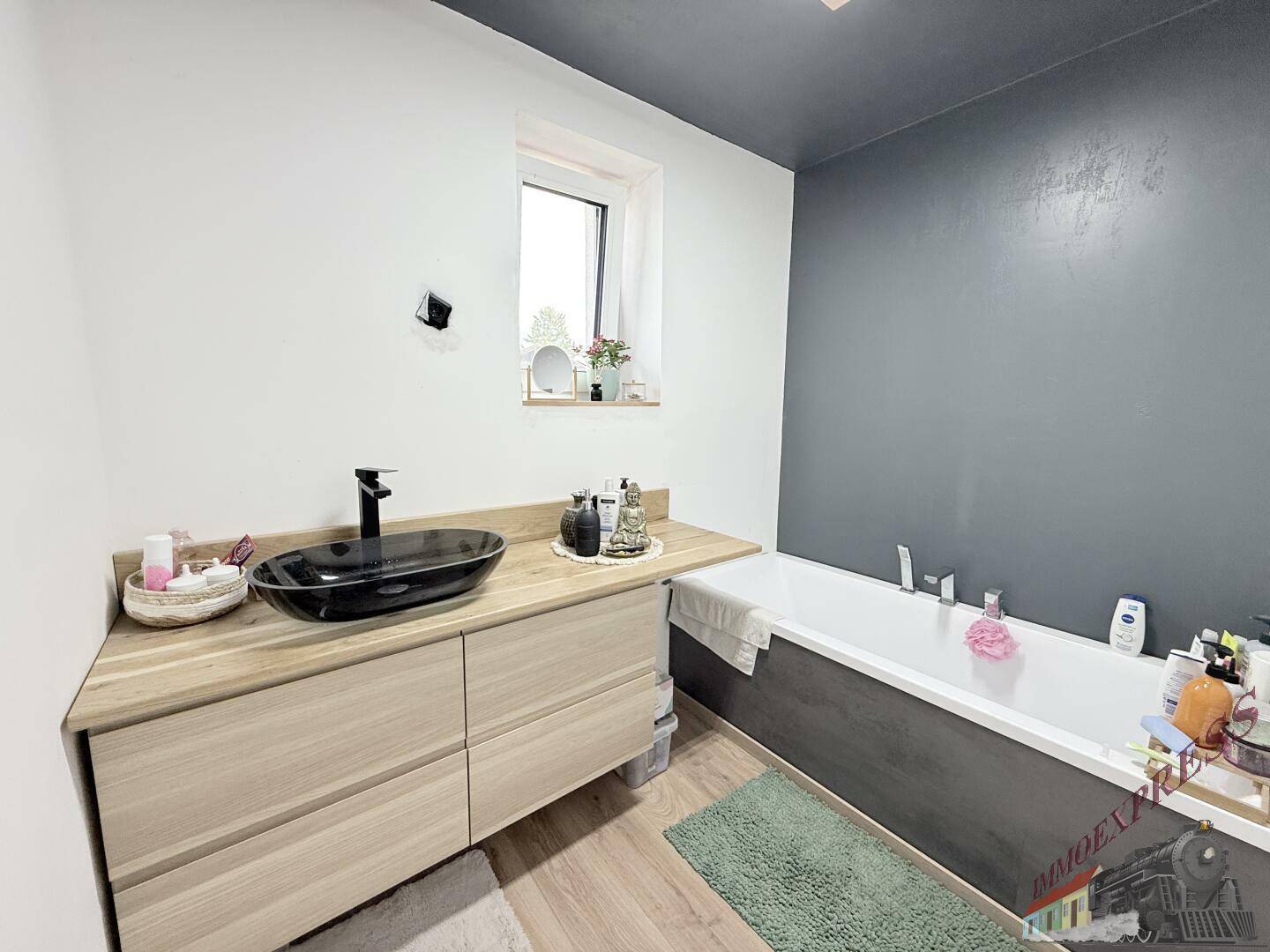 Modernes Badezimmer mit Badewanne, schwarzem Waschbecken auf Holzunterschrank und Fenster.