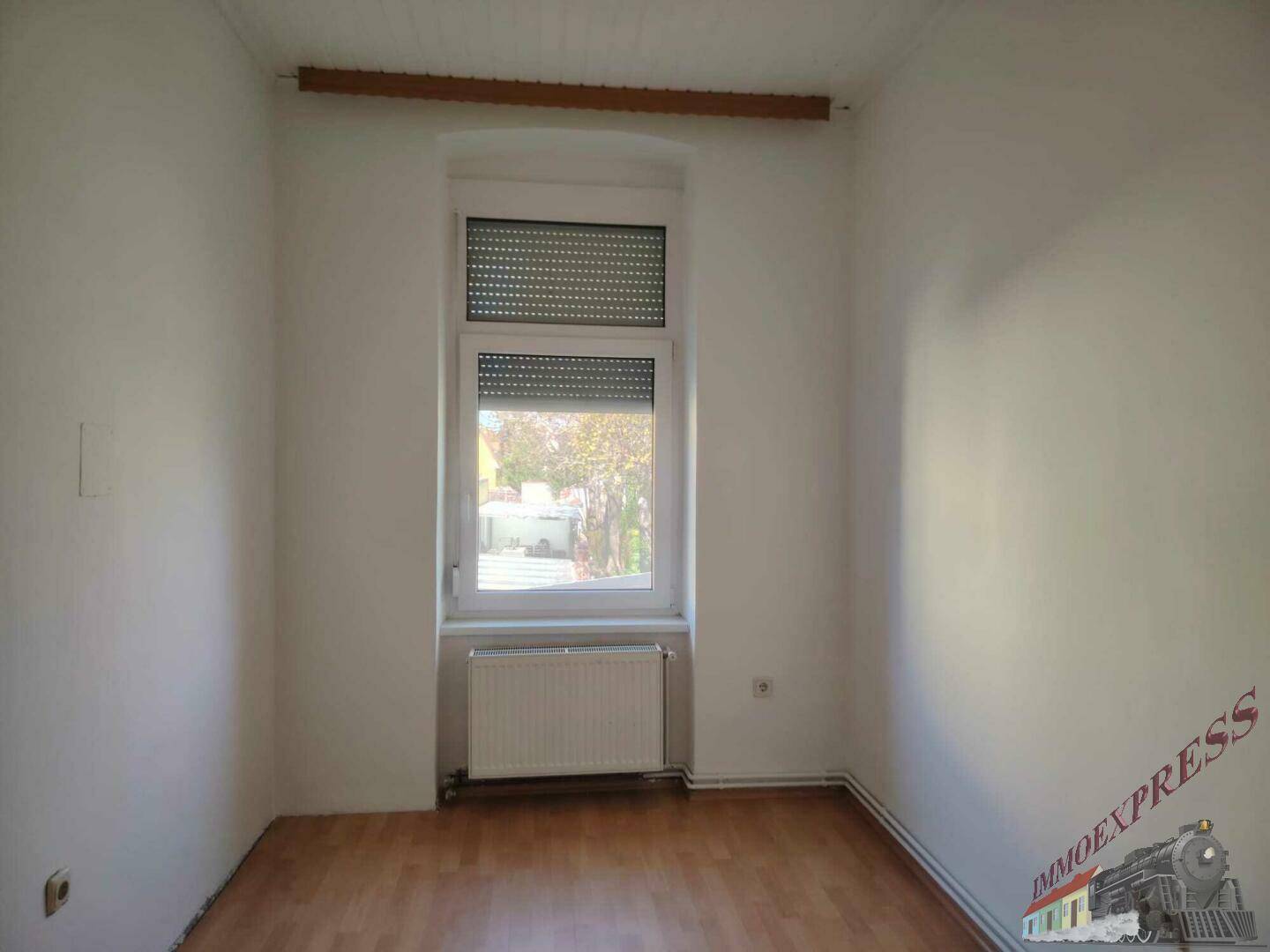 Kleineres Zimmer mit Laminatboden, einem Fenster und Heizkörper, ideal als Schlafzimmer.