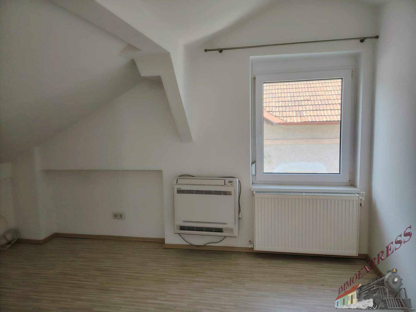 Dachzimmer mit schräger Decke, Fenster, Heizkörper und Klimaanlage, hell und geräumig.