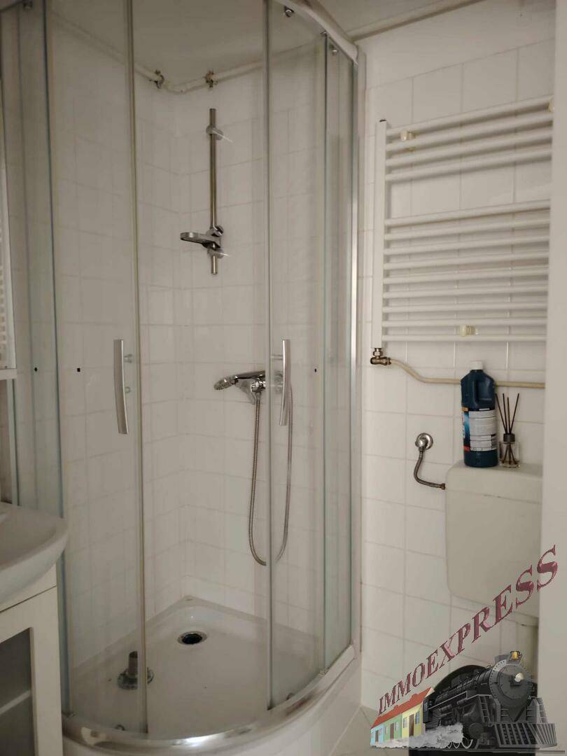 Badezimmer mit Eckduschkabine, weißen Fliesen und einem beheizten Handtuchhalter.