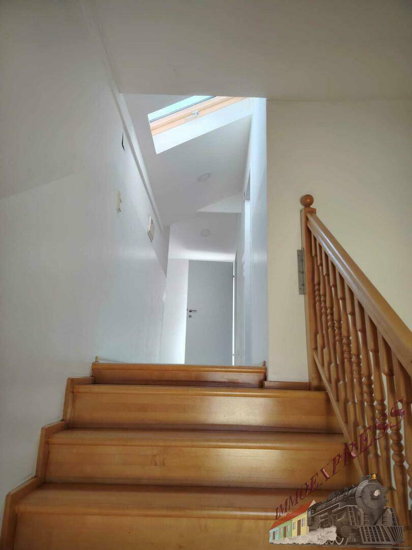 Holztreppe mit Holzgeländer führt zu einem hellen Flur mit Dachfenster.