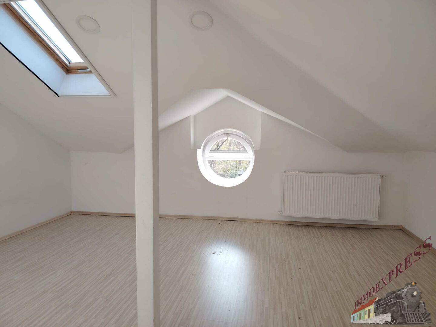 Dachzimmer mit schrägen Wänden, einem runden Fenster und einem Dachfenster für viel Licht.