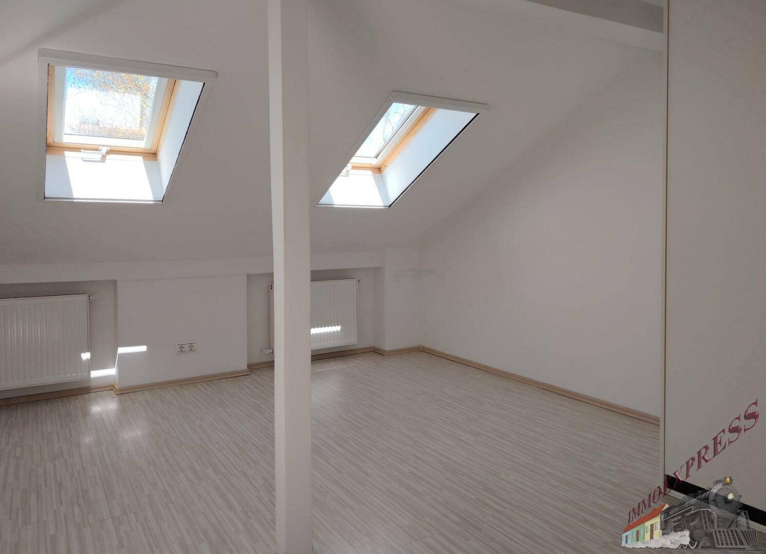 Helles Dachzimmer mit schrägen Decken und zwei Dachfenstern, bietet viel Tageslicht.