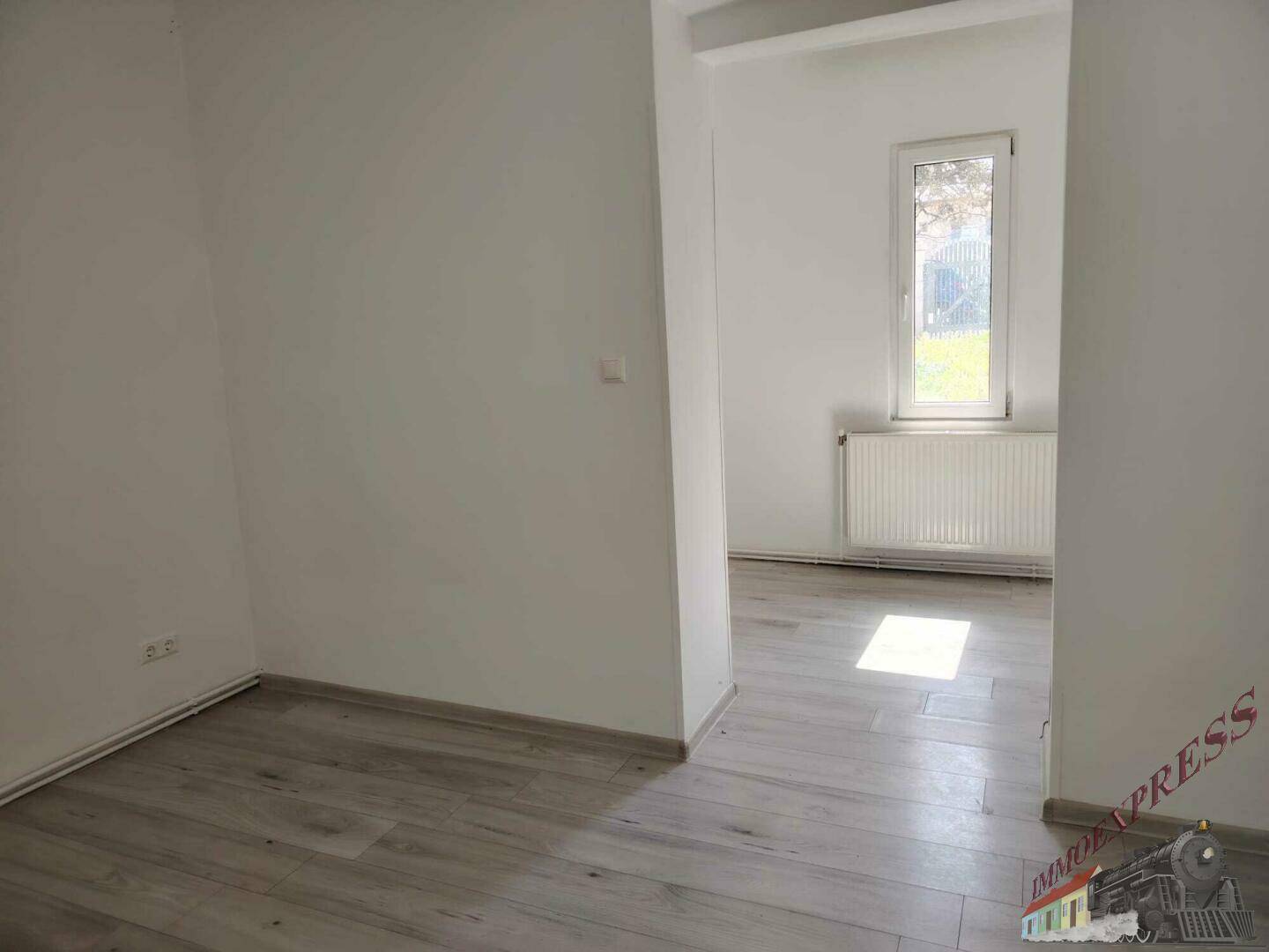 Helles Zimmer mit Laminatboden und offenem Übergang zu einem weiteren Raum.