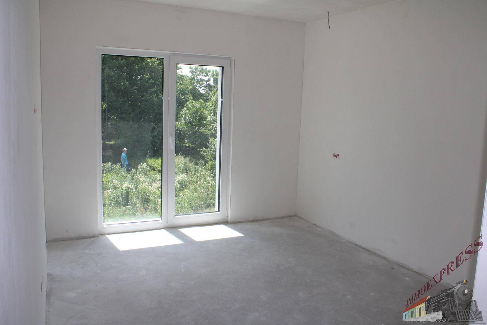 Unfertiges Zimmer mit großem Fenster und Zugang nach draußen, ideal für Schlaf- oder Arbeitszimmer.