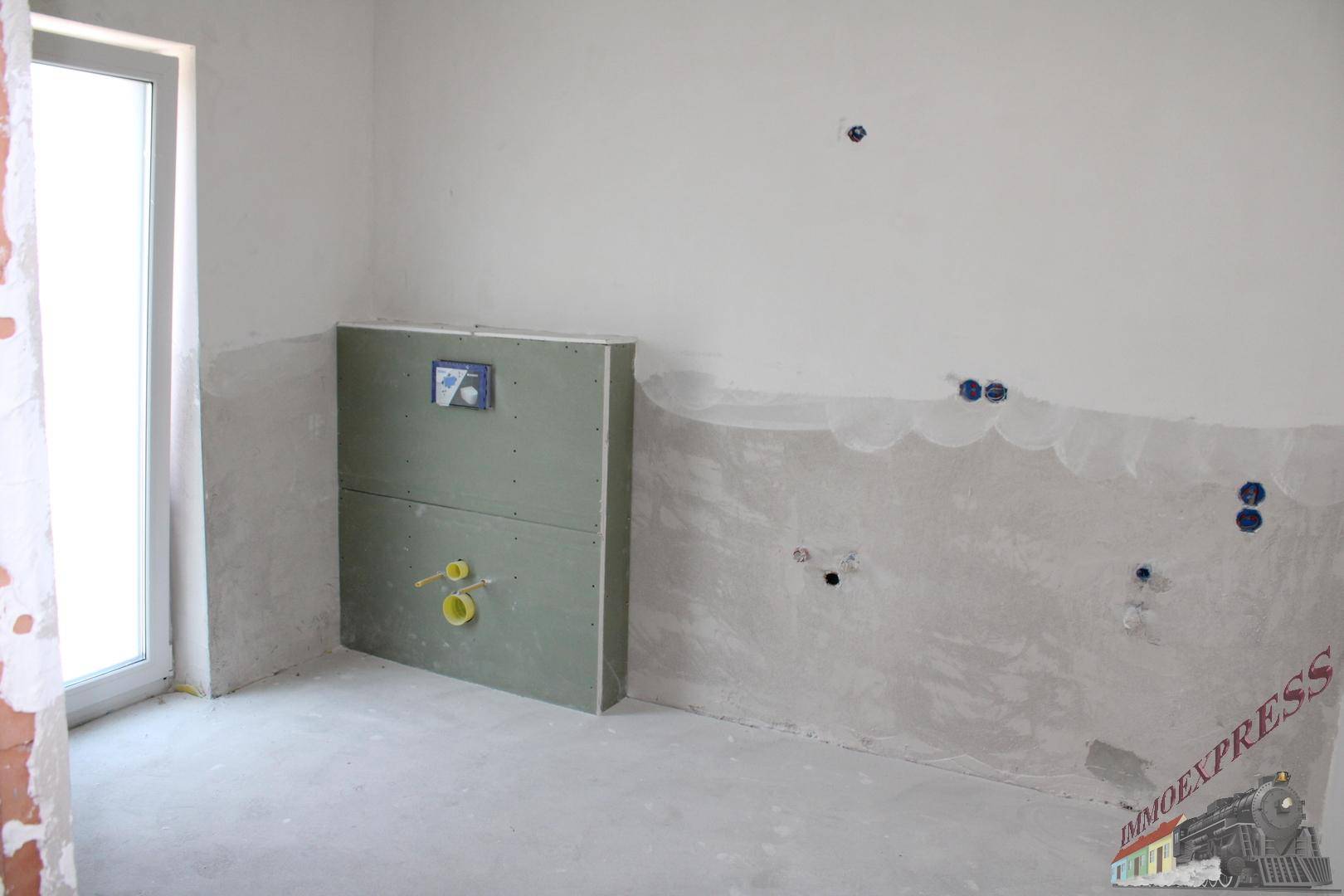 Unfertiges Badezimmer mit vorbereiteten Installationen für Toilette und Waschbecken.