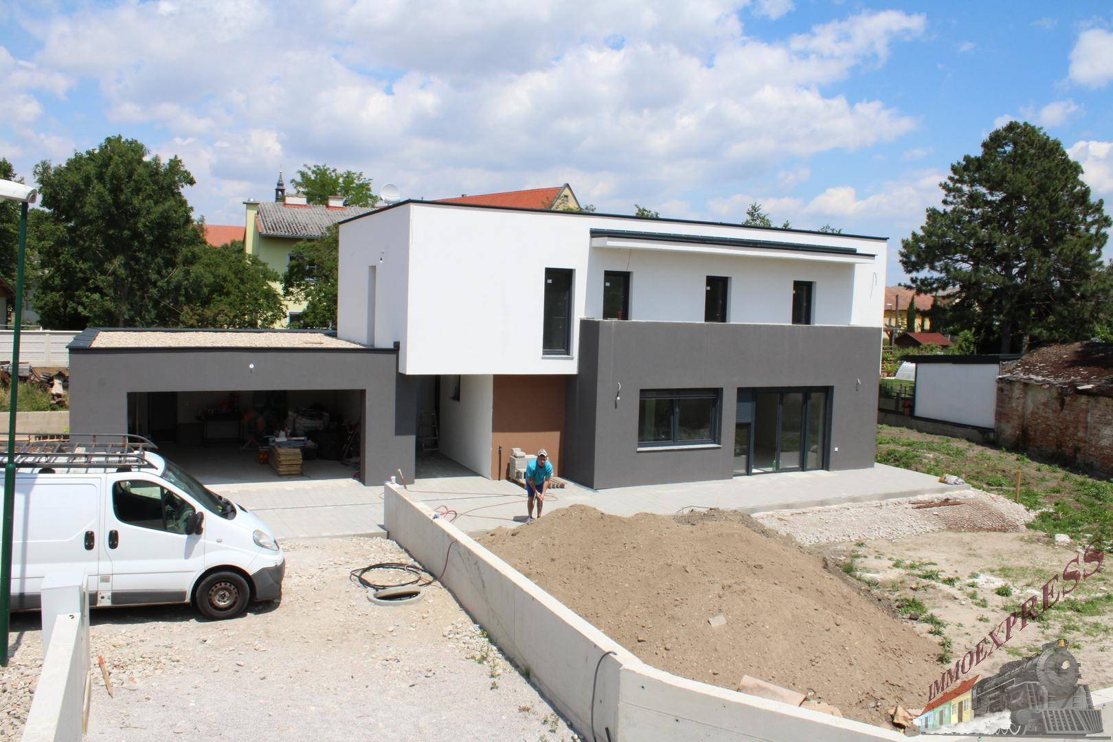 Gesamtansicht des modernen Neubaus mit weiß-grauer Fassade, großen Fenstern und Baustellenatmosphäre.