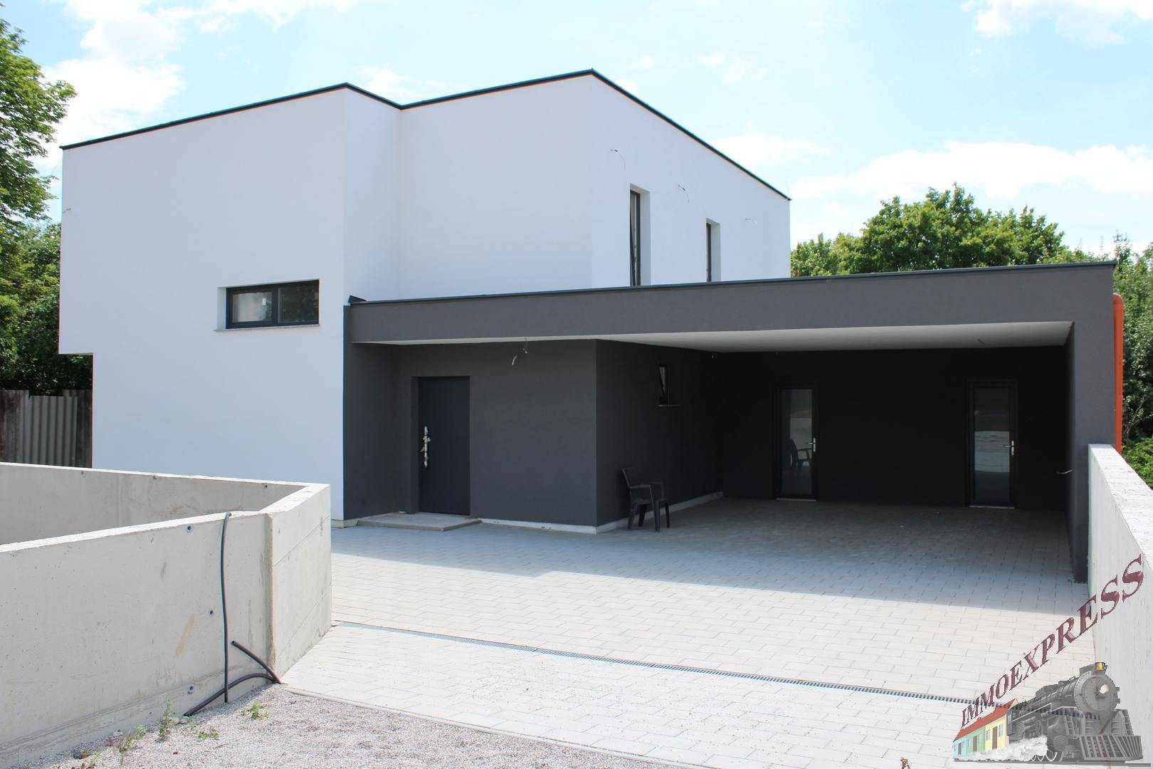 Seitenansicht des modernen Hauses mit integriertem Carport und gepflasterter Zufahrt.