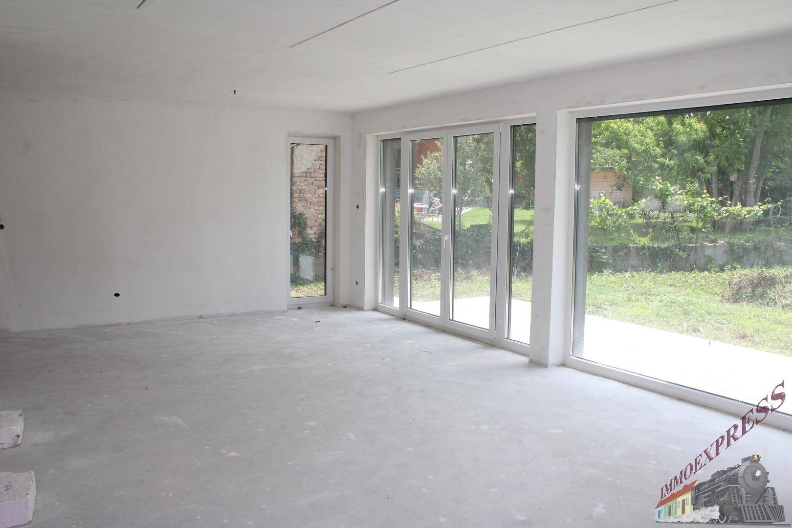 Heller, unfertiger Wohnbereich mit großen Fensterfronten und Blick ins Grüne.