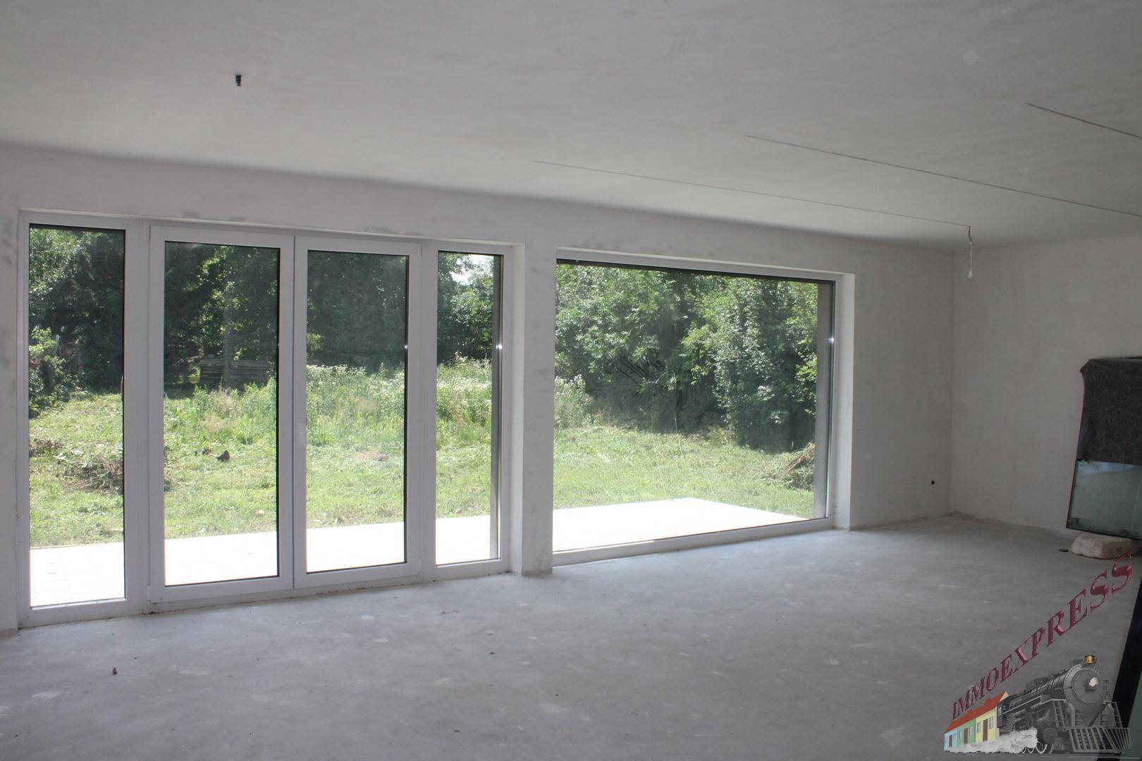 Geräumiger, unfertiger Innenraum mit breiten Fensterfronten, die viel Tageslicht hereinlassen.