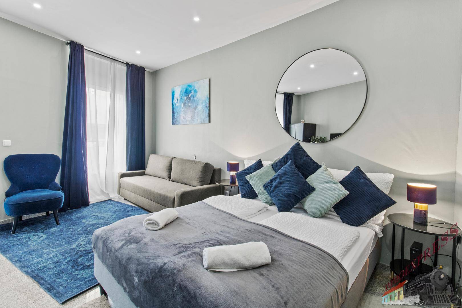 Schlafzimmer mit Doppelbett, Schlafsofa, blauen Vorhängen und Zugang zu einem Balkon oder einer Terrasse.