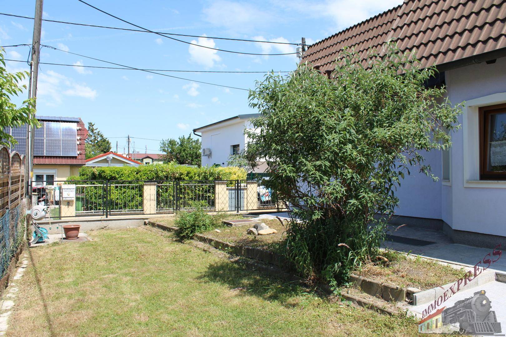 Seitlicher Gartenbereich mit Rasenfläche, kleinem Baum und einem Zaun.