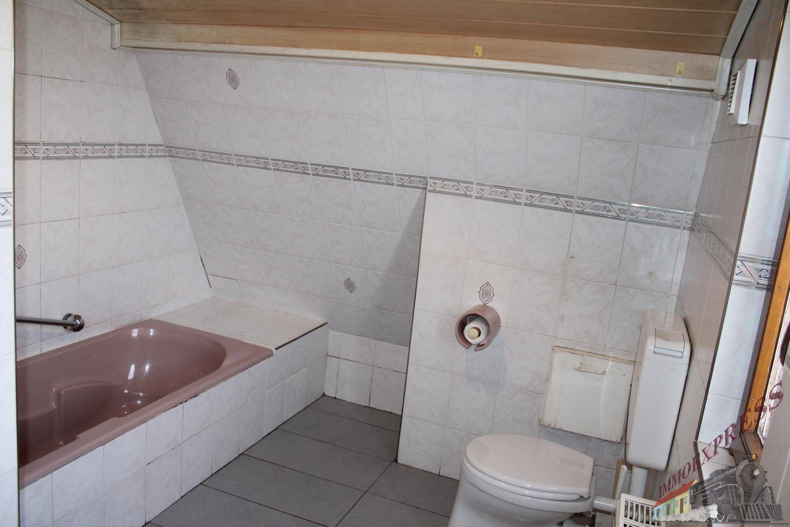 Badezimmer im Dachgeschoss mit Toilette, rosa Badewanne und schräger Decke.
