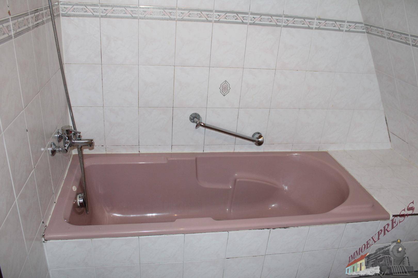 Badezimmer mit rosa Badewanne und weißen Fliesen, ausgestattet mit Haltegriff für Sicherheit.
