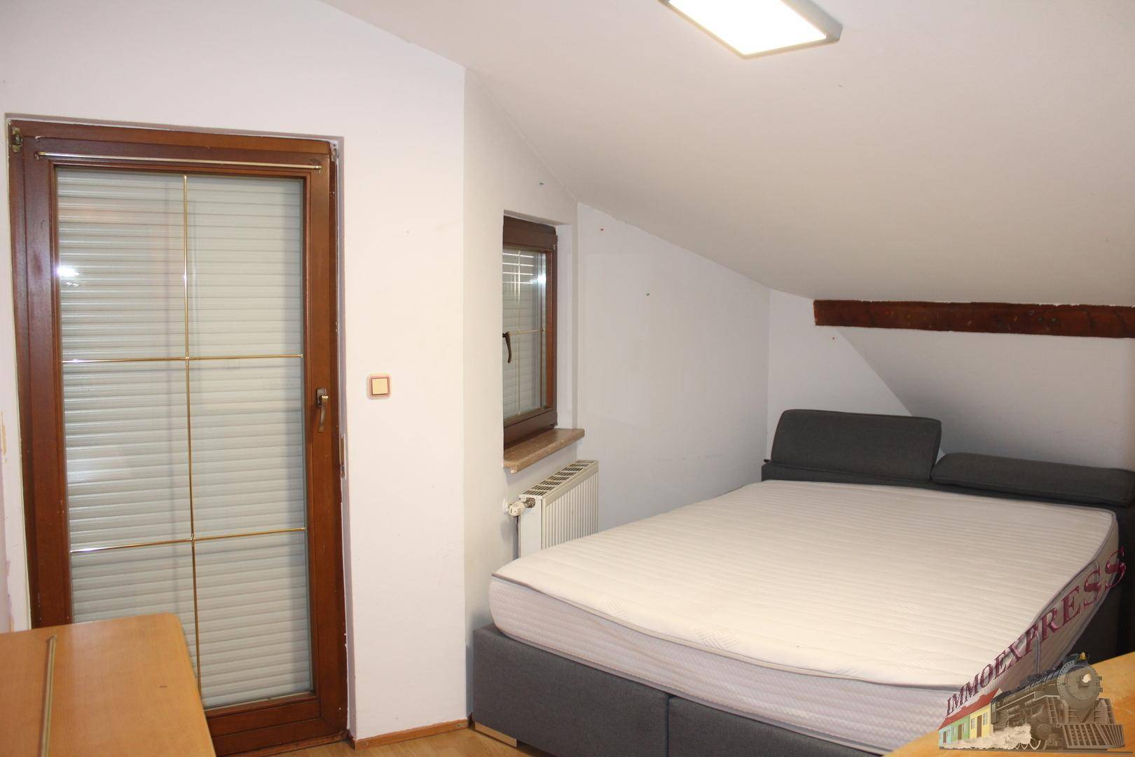 Schlafzimmer im Dachgeschoss mit schrägen Decken, Holzbalken und Zugang zum Balkon.