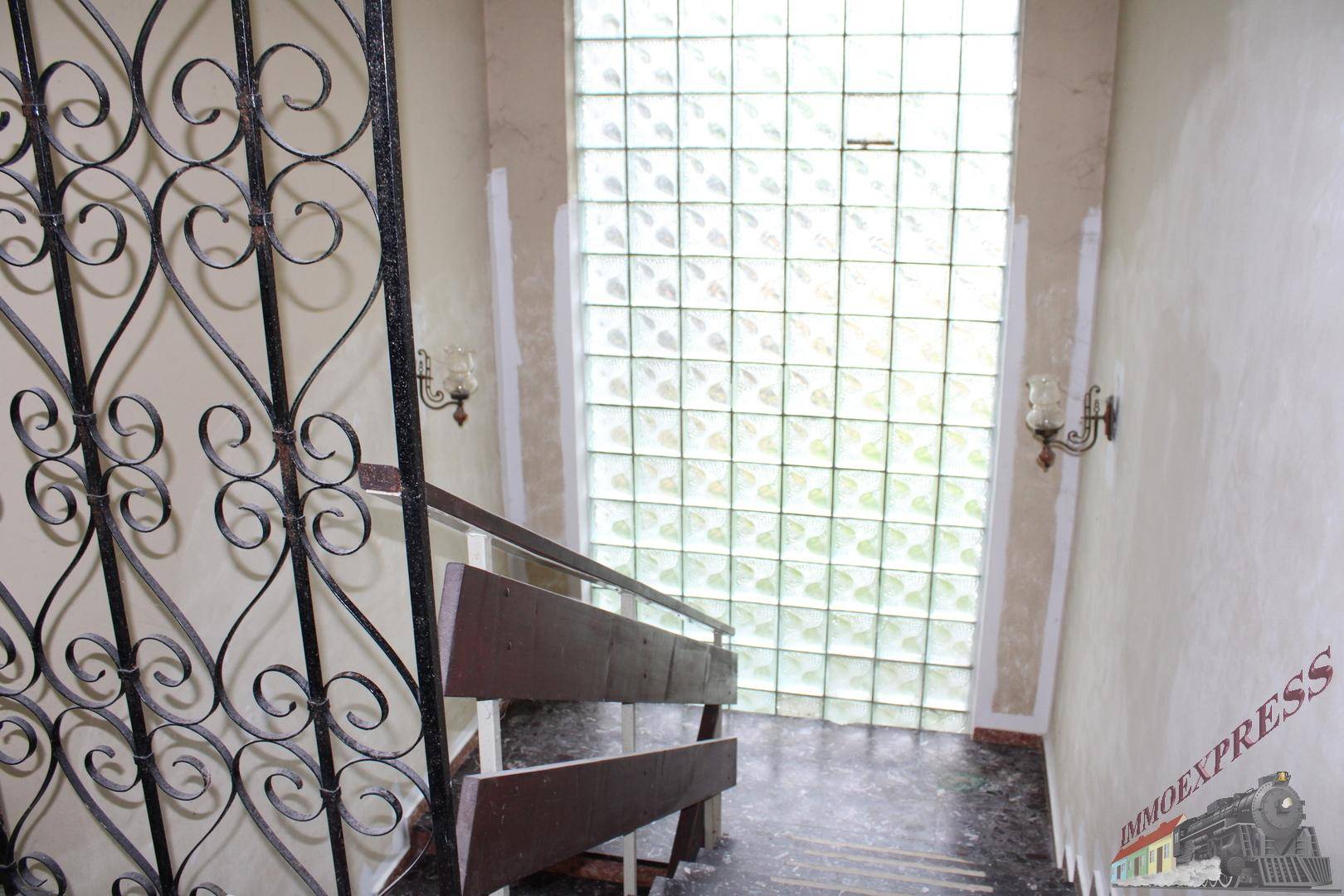Treppenhaus mit schmiedeeisernem Geländer und einer großen Glasbausteinwand für natürliches Licht.