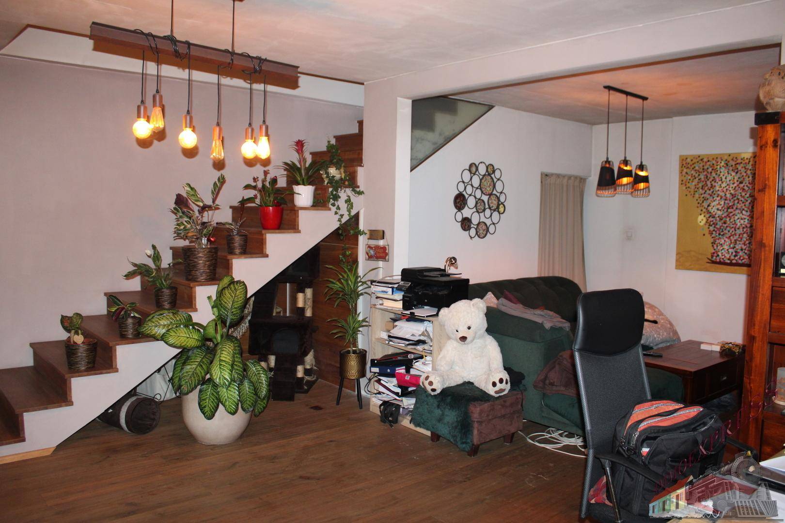 Geräumiges Wohnzimmer mit Holztreppe, vielen Pflanzen und gemütlicher Sitzecke.