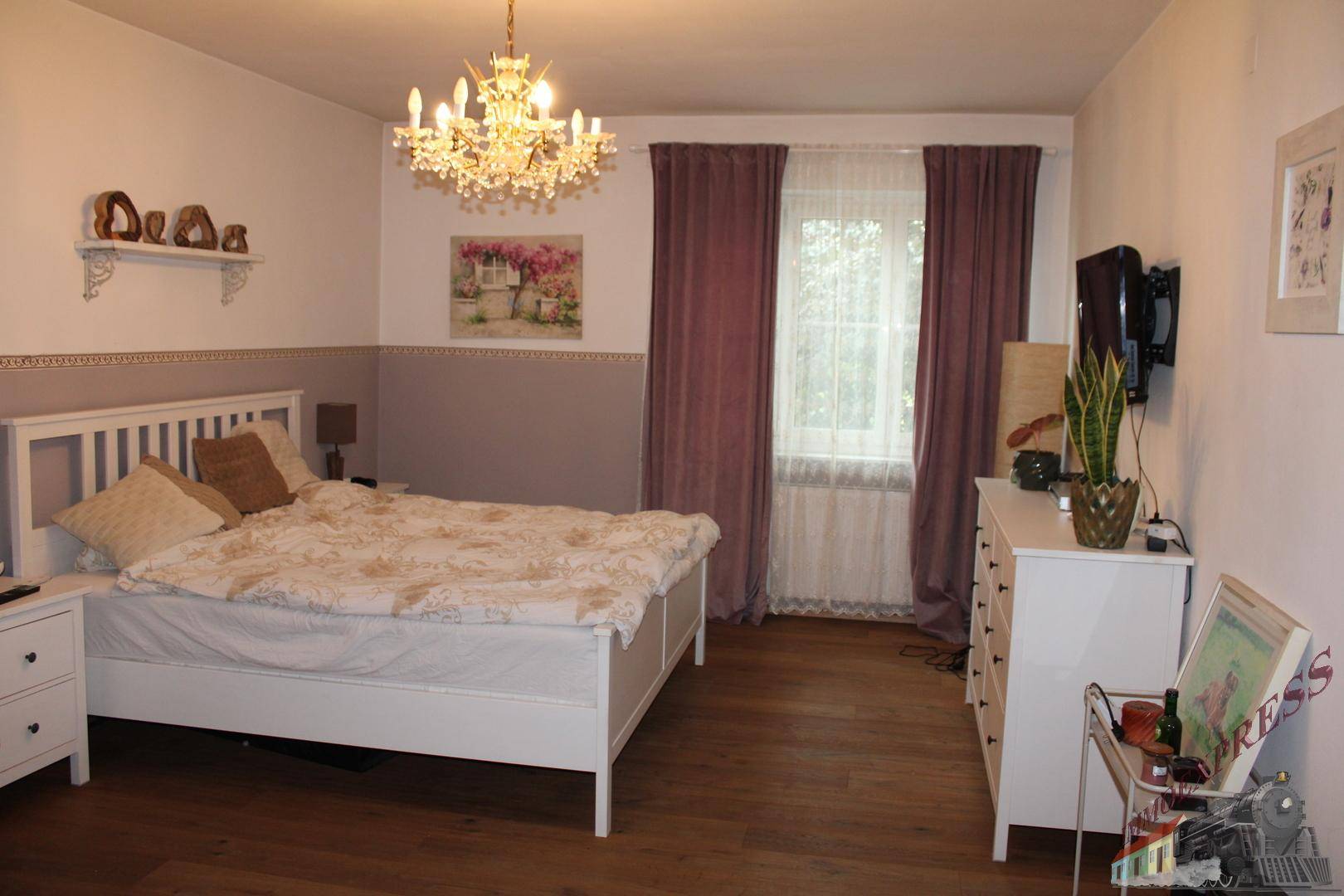 Helles Schlafzimmer mit Doppelbett, Holzboden und einem Kronleuchter an der Decke.