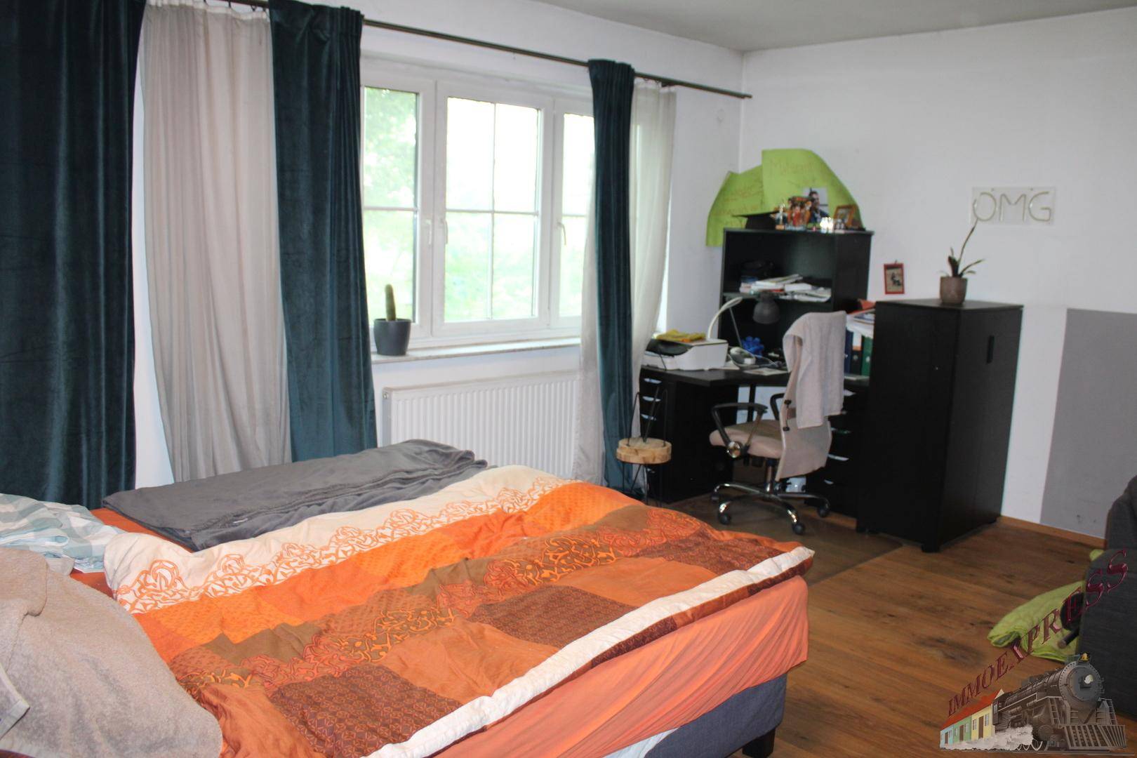 Schlafzimmer mit Holzboden, Schreibtisch und großem Fenster, ideal für Kinder oder Gäste.