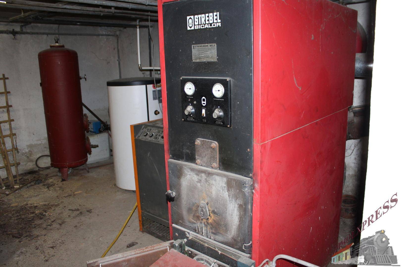Heizungsraum im Keller mit großem roten Heizkessel und Warmwasserspeicher.