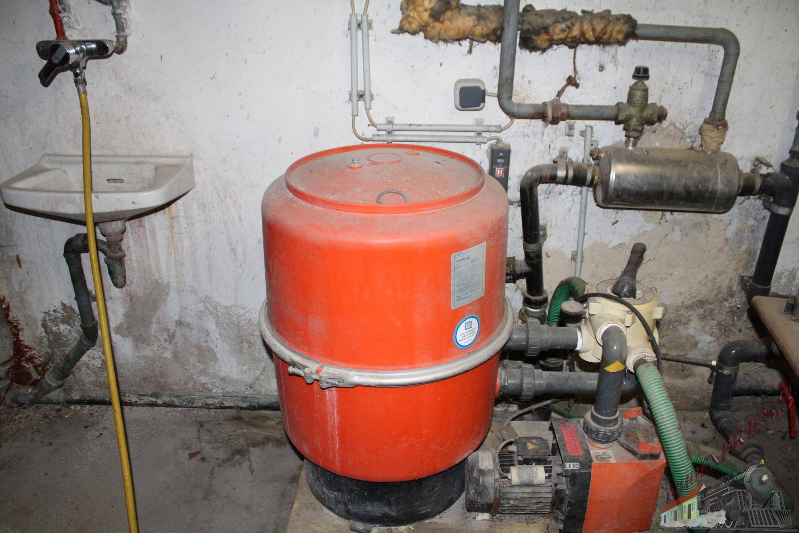 Kellerraum mit Wasserpumpe, Druckbehälter und verschiedenen Rohrleitungen.