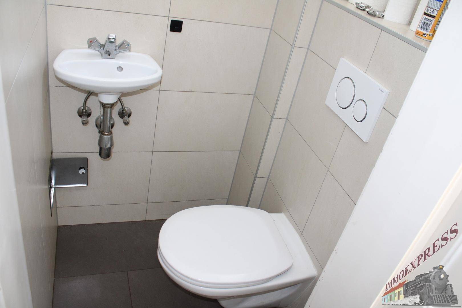 Kleines Gäste-WC mit wandhängender Toilette, kleinem Waschbecken und hellen Wandfliesen.